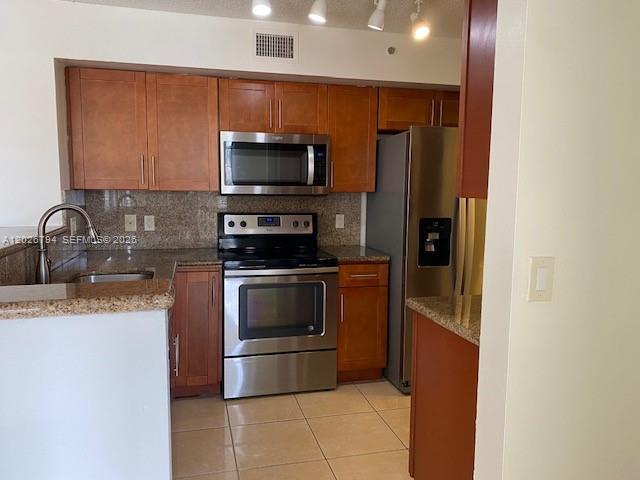 A kitchen features wood cabinets, stainless steel appliances, and light-colored tile flooring — 2051 Renaissance Blvd # 206, Miramar FL 33025, MIRAMAR, FL