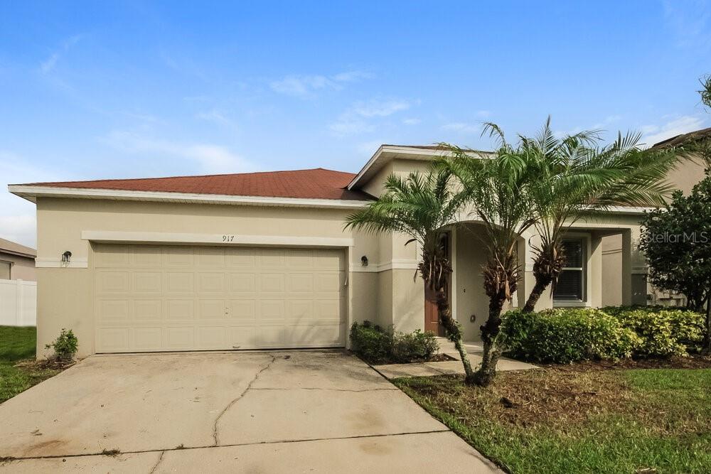 A beige single-story house features a two-car garage, a red roof, and a palm tree — 917 ANCHORAGE LANE, KISSIMMEE, FL
