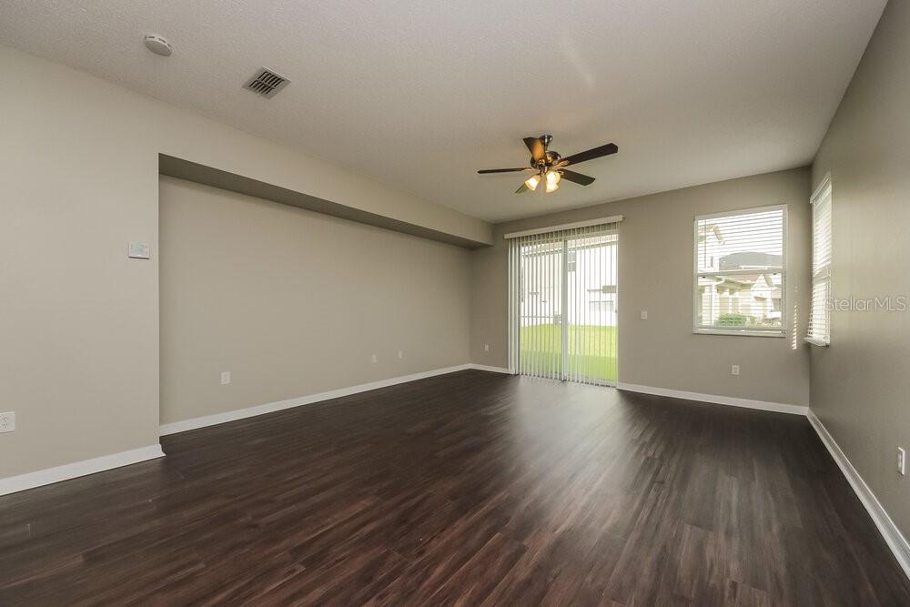 An empty living room features dark wood-look flooring, light walls, and sliding glass patio doors — 917 ANCHORAGE LANE, KISSIMMEE, FL