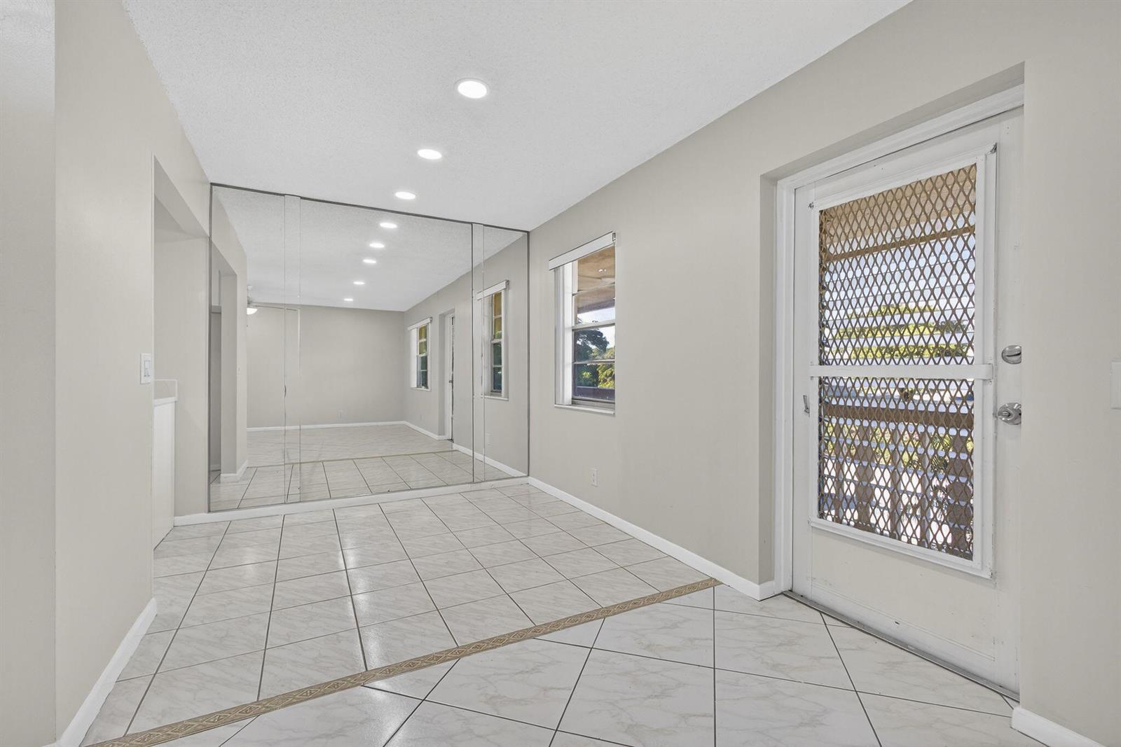 A room with light-colored tile floors, a mirrored wall, and a white exterior door — 149 Hastings I, West Palm Beach FL 33417, WEST PALM BEACH, FL