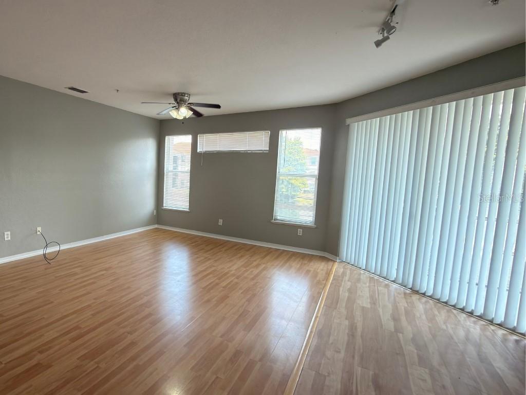 An empty living room features light wood-look flooring, gray walls, a ceiling fan, and large windows — 2525 MAITLAND CROSSING WAY UNIT 202, ORLANDO, FL