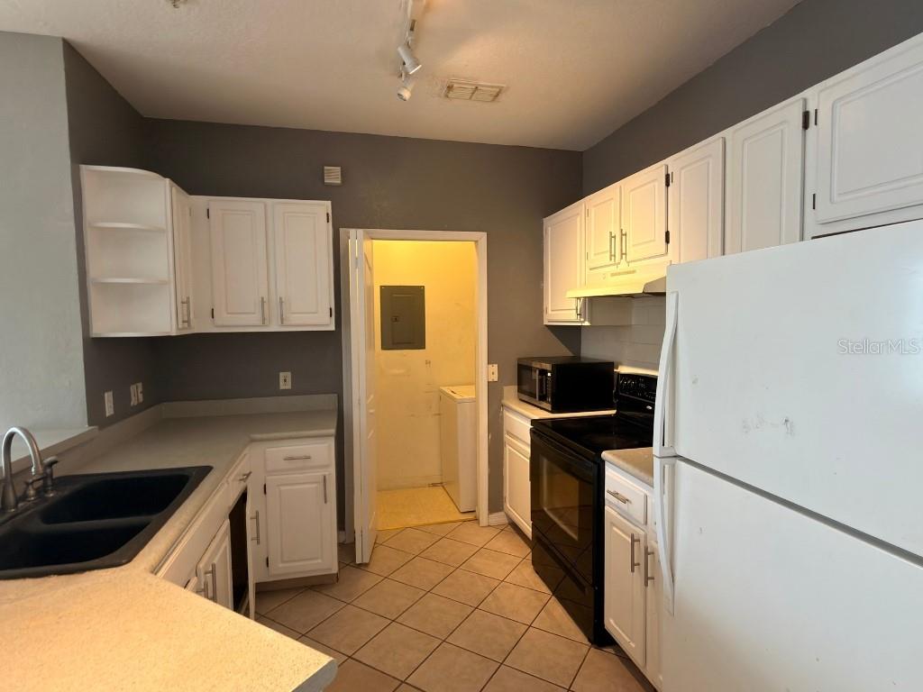 A kitchen features white cabinets, dark countertops, black appliances, and tile flooring — 2525 MAITLAND CROSSING WAY UNIT 202, ORLANDO, FL