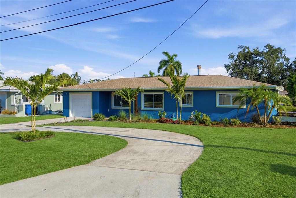 A blue single-story house with a white garage door and a curved concrete driveway — 9460 TREASURE LANE NE, ST PETERSBURG, FL