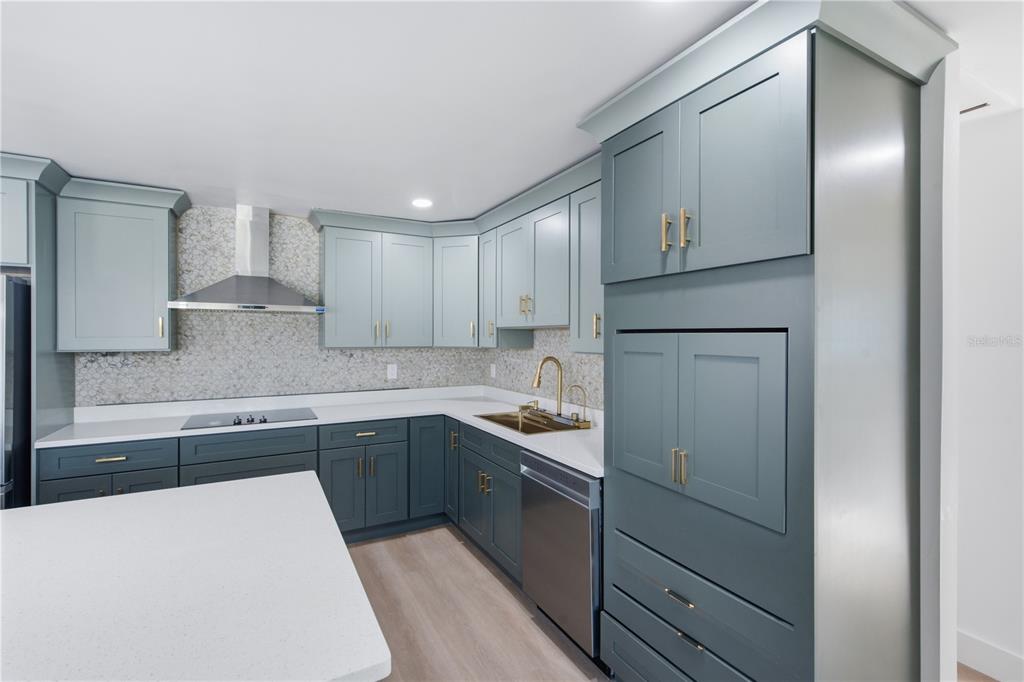 A modern kitchen features blue-grey cabinetry, white countertops, a stainless steel range hood, and gold hardware — 9460 TREASURE LANE NE, ST PETERSBURG, FL