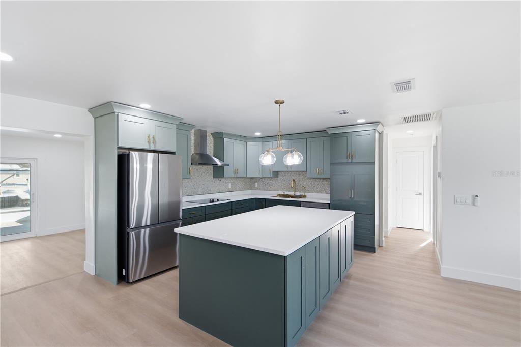 A kitchen features blue-green cabinetry, a large white-topped island, and light wood-look flooring — 9460 TREASURE LANE NE, ST PETERSBURG, FL