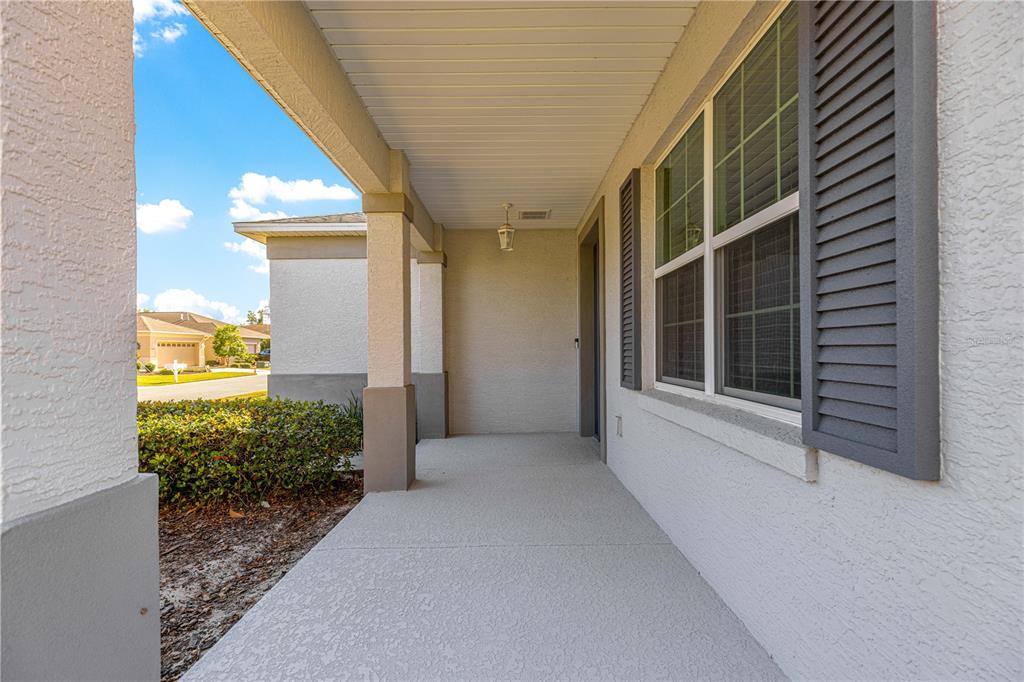 A covered concrete porch features a support pillar, a window with gray shutters, and a light — 8546 SW 79TH AVENUE, OCALA, FL