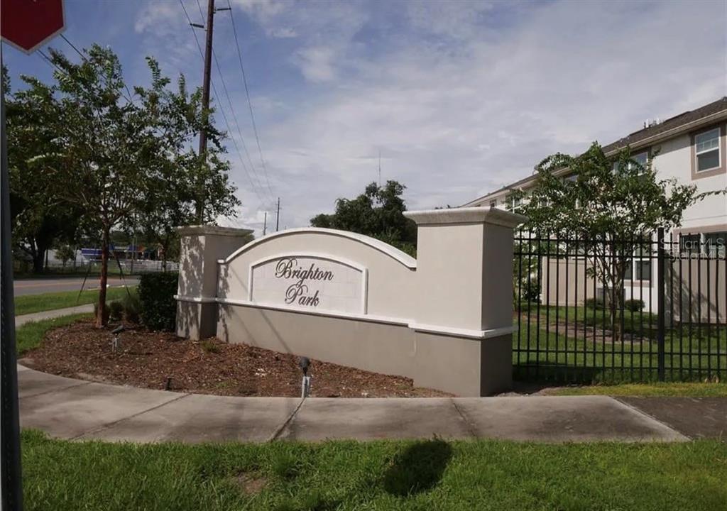 A beige monument sign for Brighton Park stands near a sidewalk and black metal fence — 3778 BRIGHTON PARK CIRCLE, ORLANDO, FL