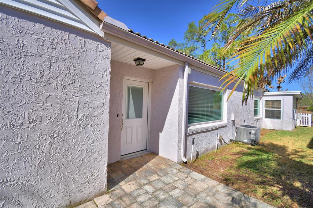 A white front door with a glass panel sits under a covered entryway with pavers — 447 SAN JOSE DRIVE, WINTER HAVEN, FL
