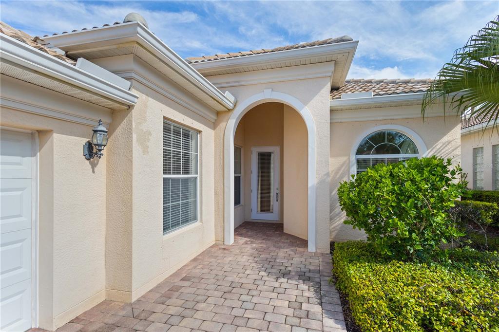 A paved walkway leads to the arched entryway of a beige stucco house with tile roofing — 13180 IPOLITA STREET, VENICE, FL