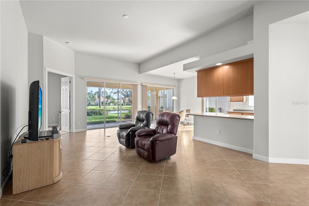 A living room with tile flooring, two recliners, and a view of a pond outside — 13180 IPOLITA STREET, VENICE, FL