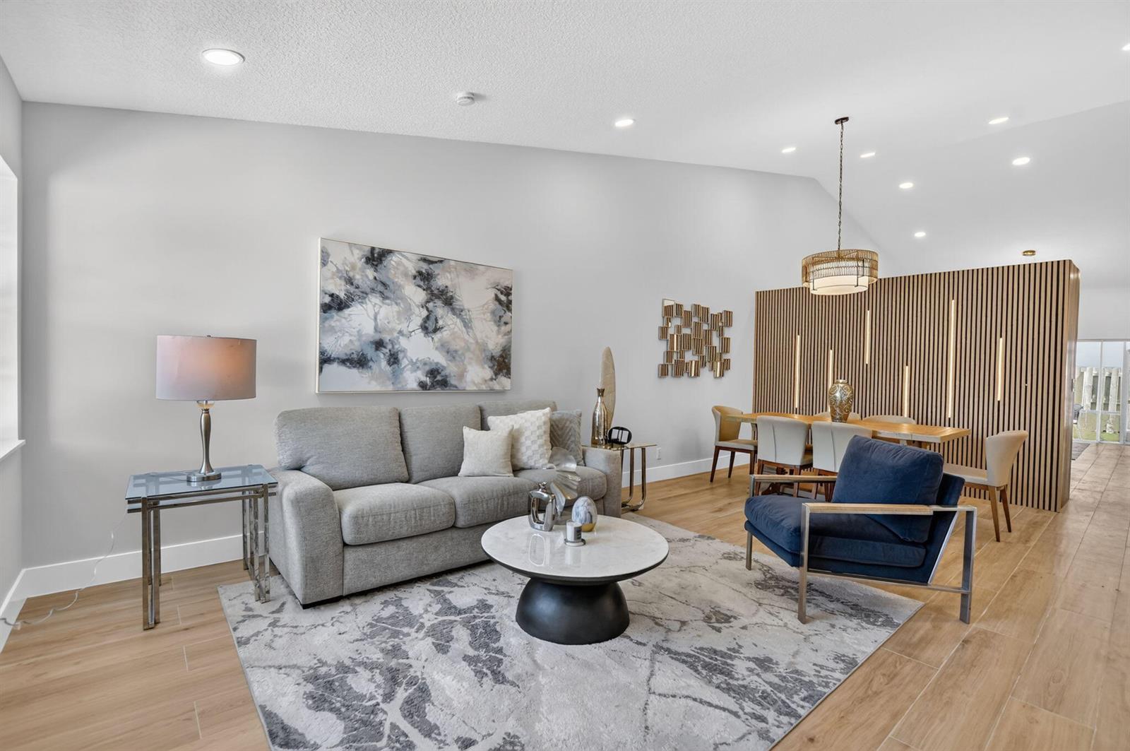 A living and dining area features light wood floors, a gray sofa, and wood-slatted walls — 11213 Jasmine Hill Circle, Boca Raton FL 33498, BOCA RATON, FL