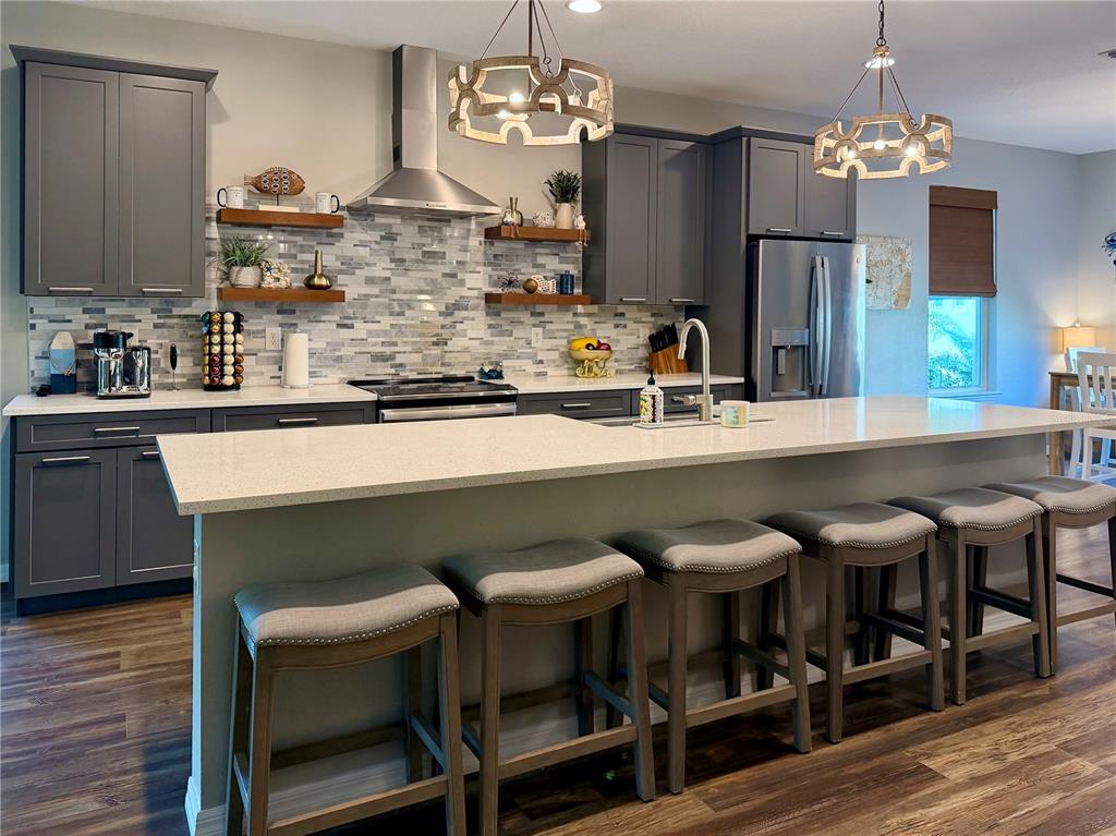 A modern kitchen features gray cabinets, a quartz island with bar seating, and tile backsplash — 849 CALLISTA CAY LOOP, TARPON SPRINGS, FL