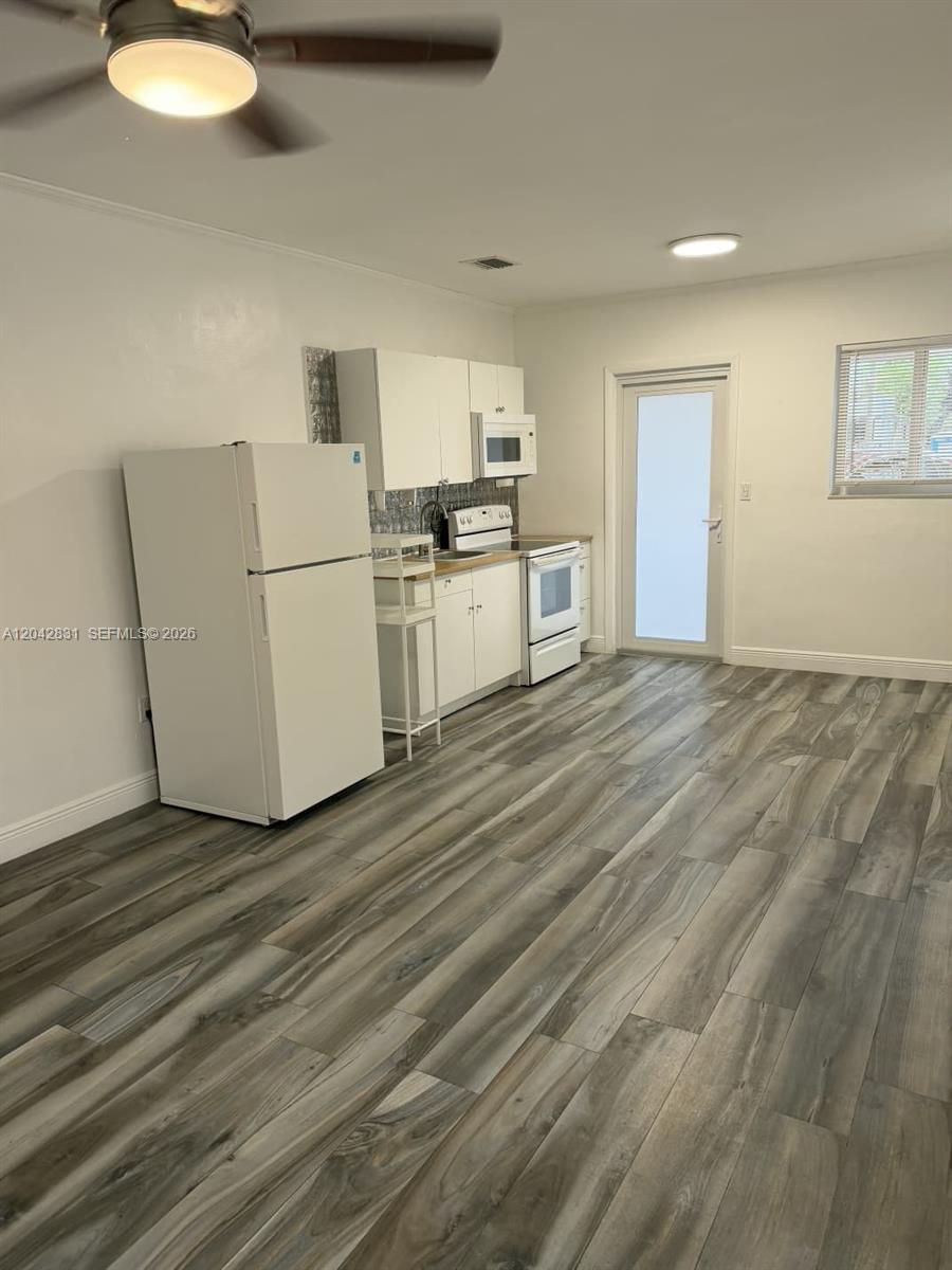 This kitchen features white cabinets, a white refrigerator, a stove, and wood-look flooring — 3115 NW 23rd Ave # 0, Miami FL 33142, MIAMI, FL