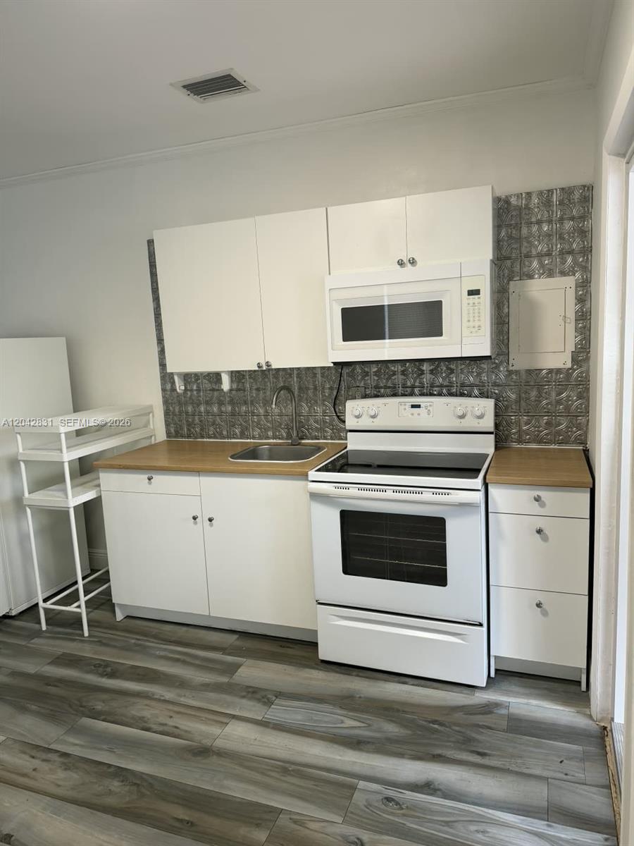 A kitchen features white cabinets, a wood countertop, a stainless steel sink, and patterned backsplash — 3115 NW 23rd Ave # 0, Miami FL 33142, MIAMI, FL