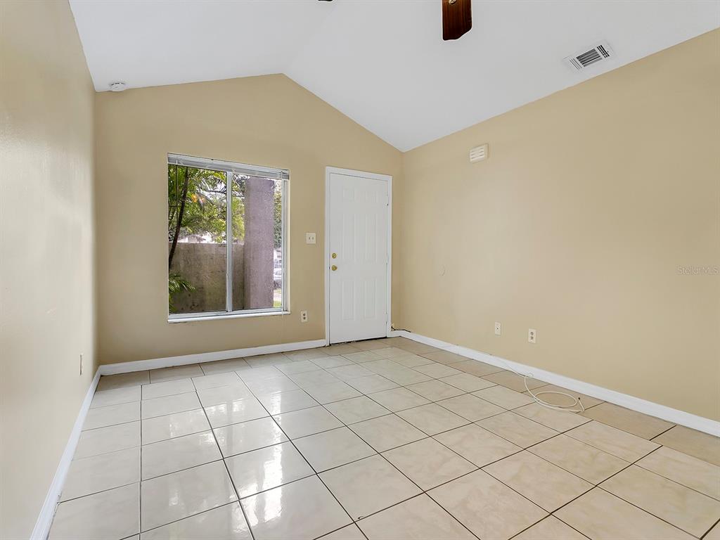 An empty room with beige walls, light-colored tile flooring, a vaulted ceiling, and a window — 10425 RIVA RIDGE TRAIL, ORLANDO, FL