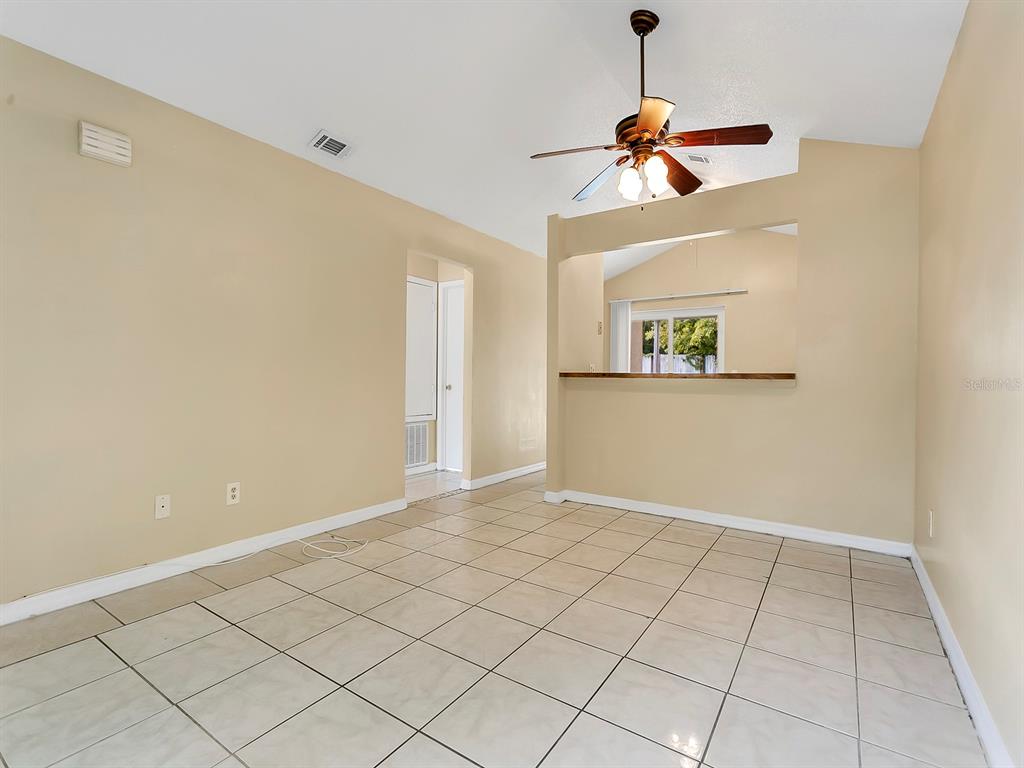 A living room with beige walls, tile flooring, a ceiling fan, and a kitchen pass-through window — 10425 RIVA RIDGE TRAIL, ORLANDO, FL