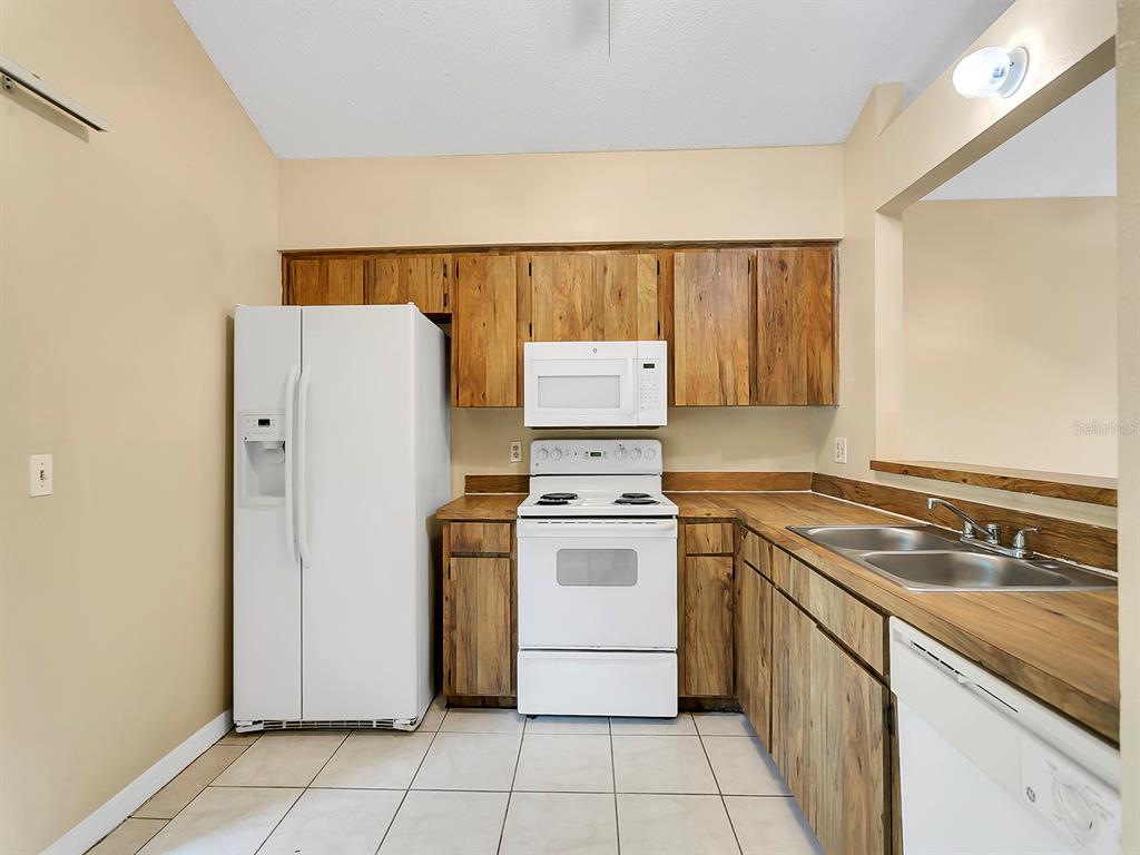 A kitchen features wood cabinets, white appliances, a double sink, and light-colored tile flooring — 10425 RIVA RIDGE TRAIL, ORLANDO, FL
