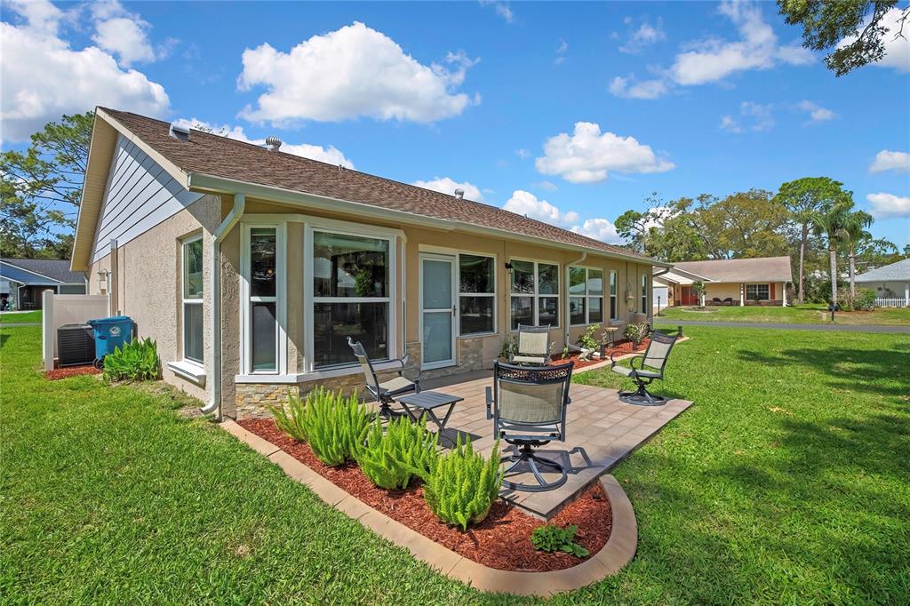 The exterior of a house features a paved patio, outdoor furniture, and a landscaped garden bed — 6433 LOST TREE LANE, SPRING HILL, FL