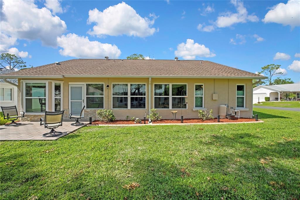 The rear exterior of a single-story house features a paved patio, lawn, and multiple windows — 6433 LOST TREE LANE, SPRING HILL, FL