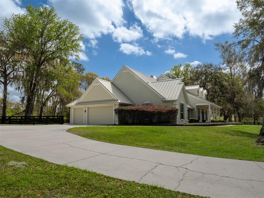 A light-colored house with a metal roof and a multi-car garage sits on a lawn — 8535 NW 136TH AVENUE ROAD, OCALA, FL
