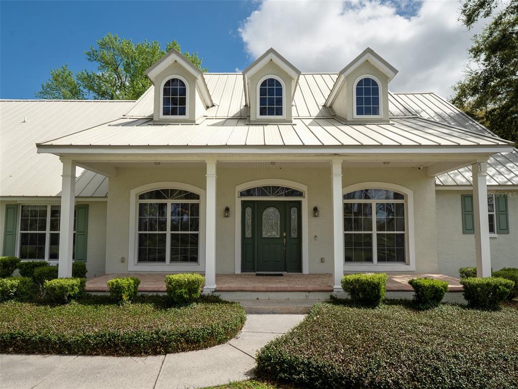 A light-colored house with a metal roof, three dormer windows, and a covered front porch — 8535 NW 136TH AVENUE ROAD, OCALA, FL
