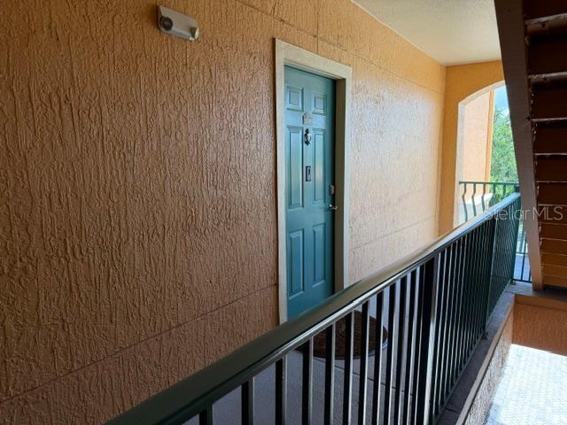 An exterior hallway features a teal door, textured orange walls, and a black metal railing — 2733 VIA CIPRIANI UNIT 820B, CLEARWATER, FL