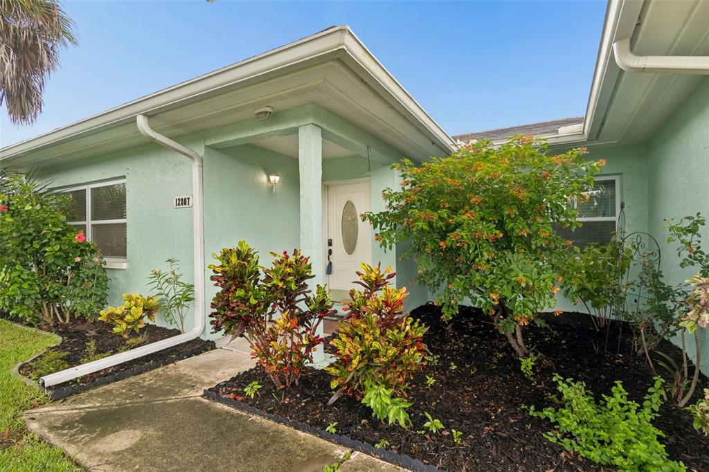 The exterior of a light green house features a front entrance and landscaped garden beds — 12807 WILLOWDALE WAY, HUDSON, FL
