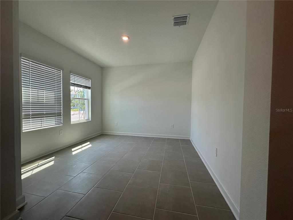 An empty room features large windows with blinds, light-colored walls, and gray tile flooring — 3052 PARK VALE ROAD, ST CLOUD, FL