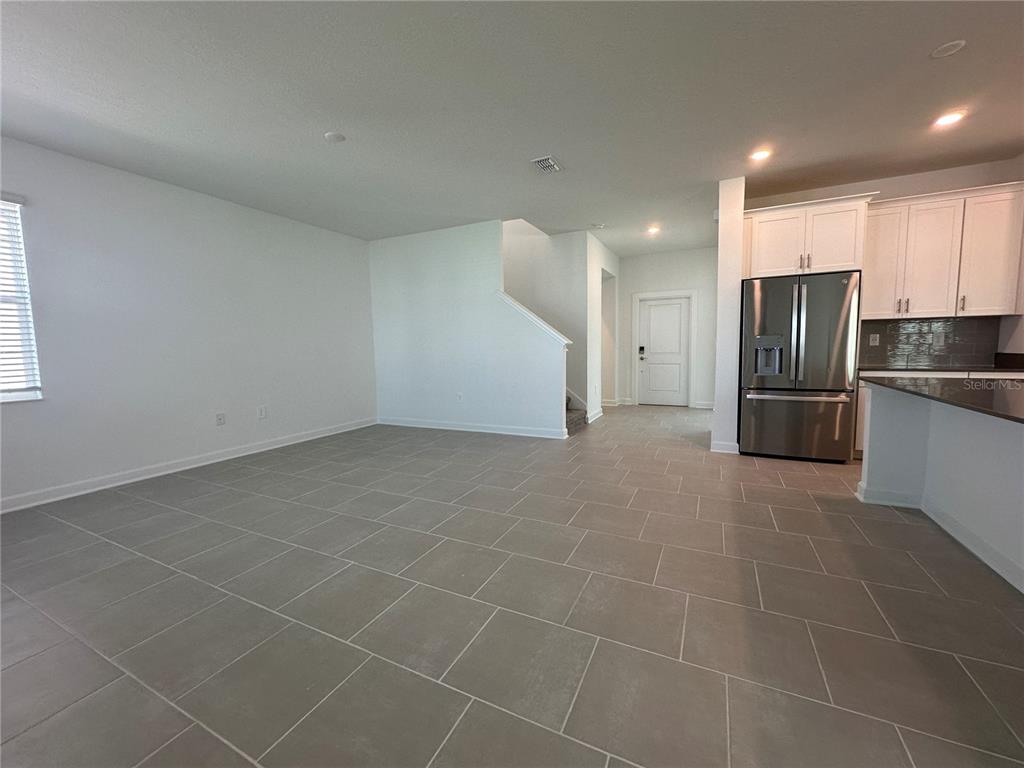 An open-concept room features gray tile flooring, white walls, and a kitchen with stainless appliances — 3052 PARK VALE ROAD, ST CLOUD, FL