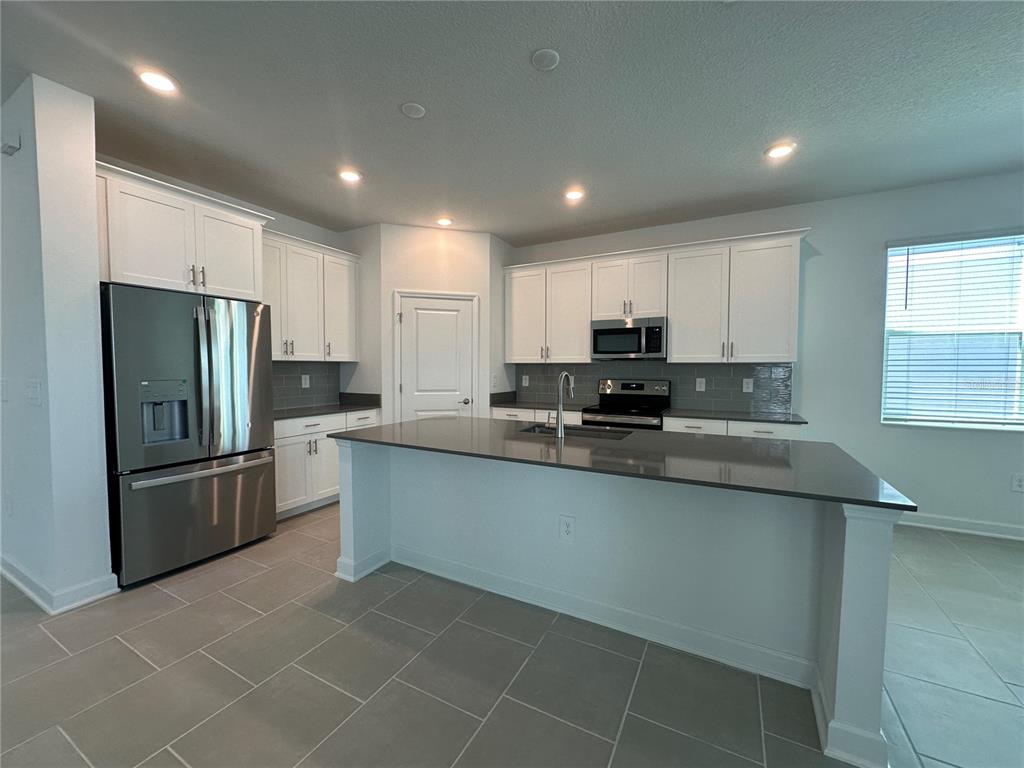 A modern kitchen features white cabinetry, gray countertops, stainless steel appliances, and tile flooring — 3052 PARK VALE ROAD, ST CLOUD, FL