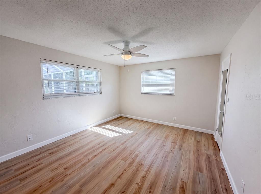 An empty bedroom features light-colored walls, wood-look flooring, two windows with blinds, and a ceiling fan — 624 SHERMAN ROAD, SOUTH DAYTONA, FL