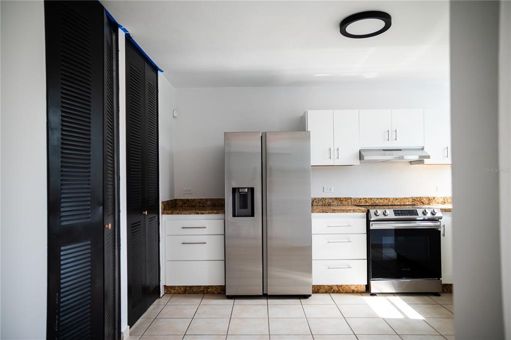 A kitchen features white cabinets, stainless steel appliances, granite countertops, and black louvered closet doors — 29 CALLE BASILIO CATALA UNIT 210, GUAYNABO, PR