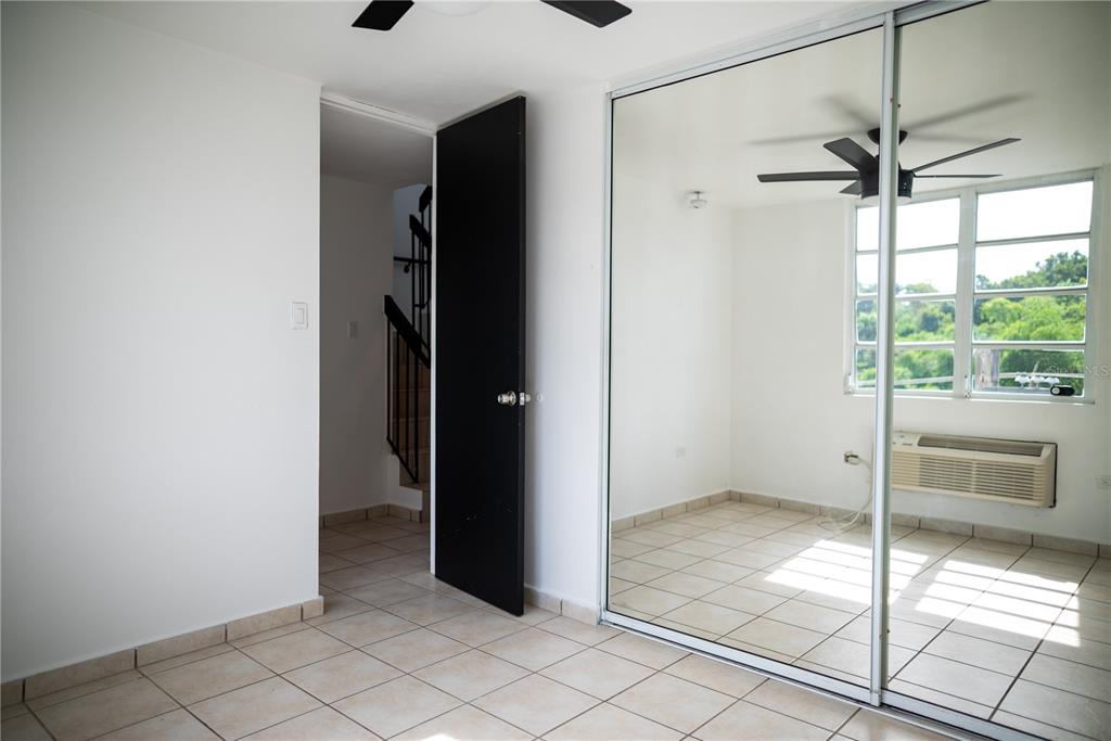 A bedroom with tiled floors, a black door, and a large mirrored sliding closet door — 29 CALLE BASILIO CATALA UNIT 210, GUAYNABO, PR