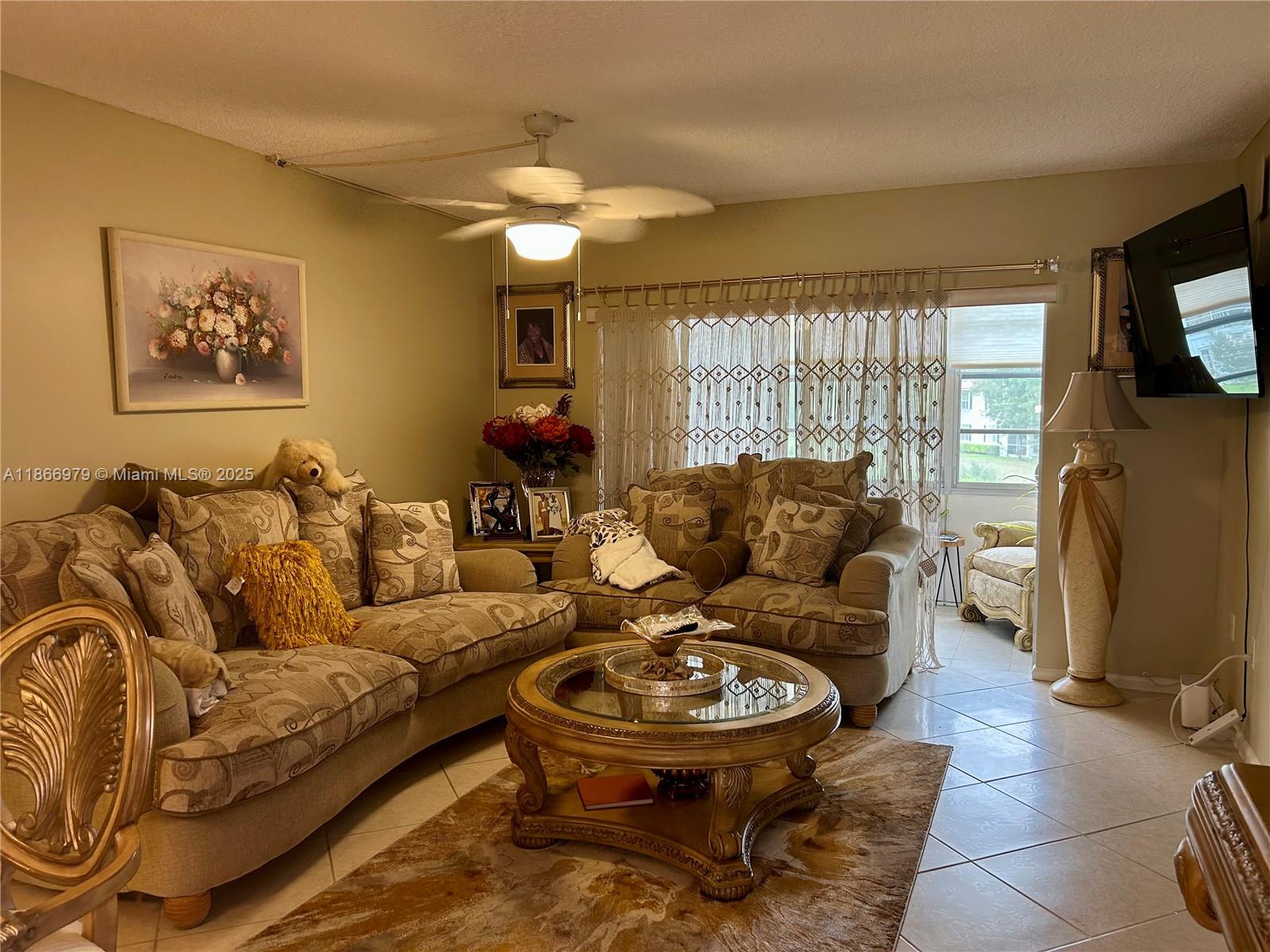 A living room features beige patterned sofas, a glass-topped coffee table, and tile flooring — 9802 Marina Blvd # 125, Boca Raton FL 33428, BOCA RATON, FL