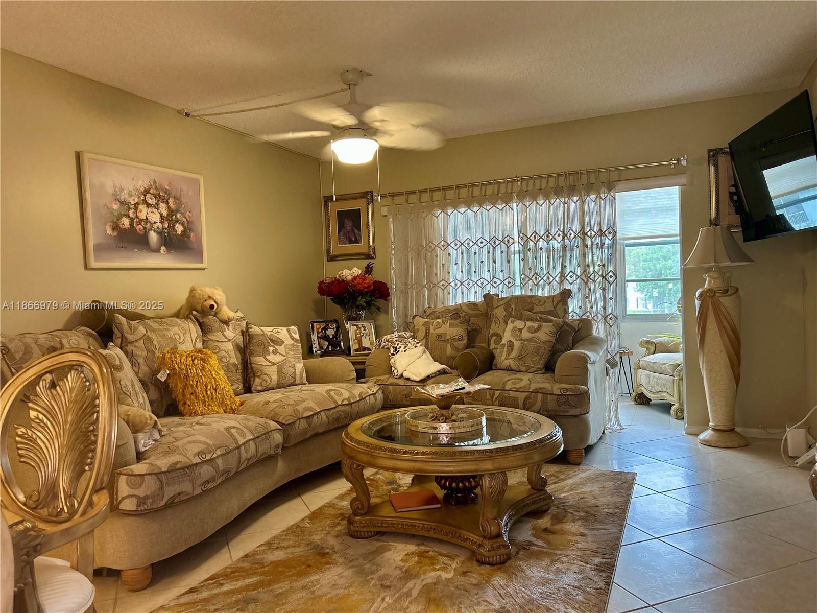 A living room features patterned sofas, a glass-topped coffee table, and a ceiling fan — 9802 Marina Blvd # 125, Boca Raton FL 33428, BOCA RATON, FL