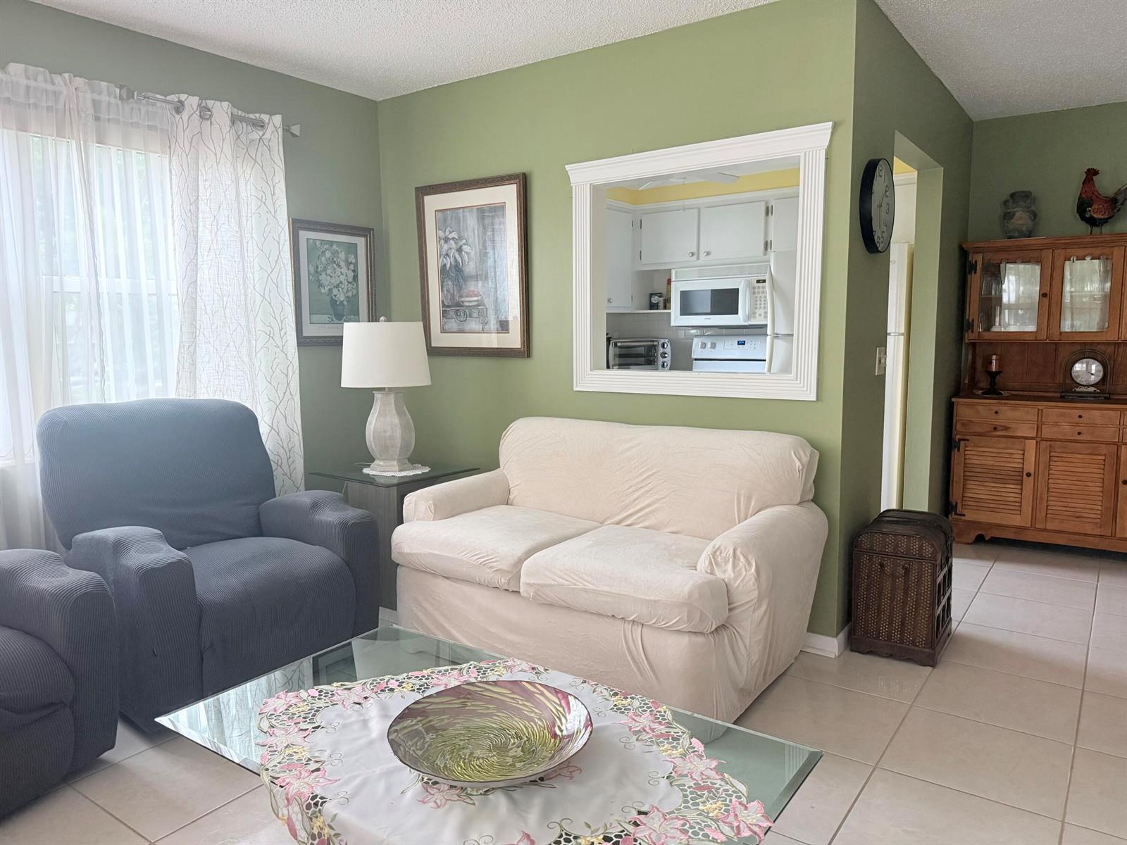 A living room with green walls, a white loveseat, a dark armchair, and a kitchen pass-through — 204 Durham D # 204, Deerfield Beach FL 33442, DEERFIELD BEACH, FL