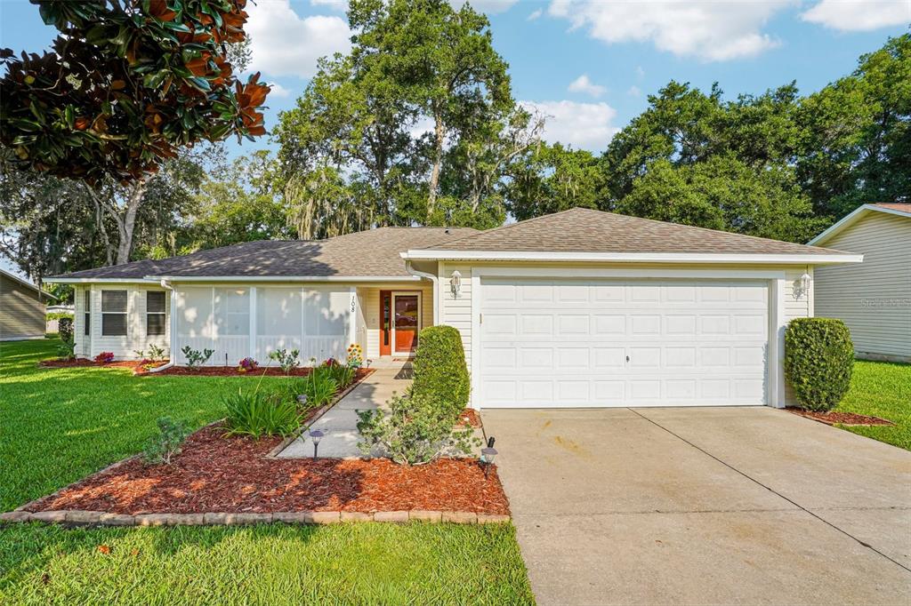 A single-story house with a white garage, a screened front porch, and a landscaped yard — 108 CHERRY BLOSSOM LANE, LADY LAKE, FL
