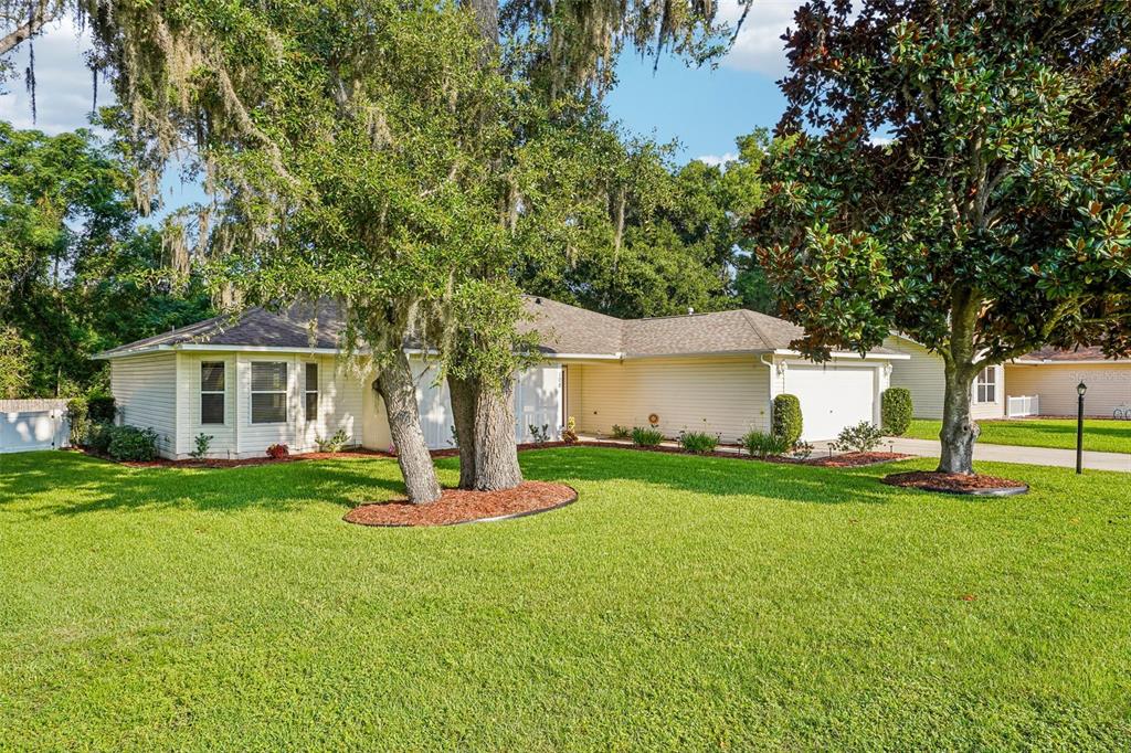 A single-story house with light siding, a two-car garage, and large trees in the front yard — 108 CHERRY BLOSSOM LANE, LADY LAKE, FL