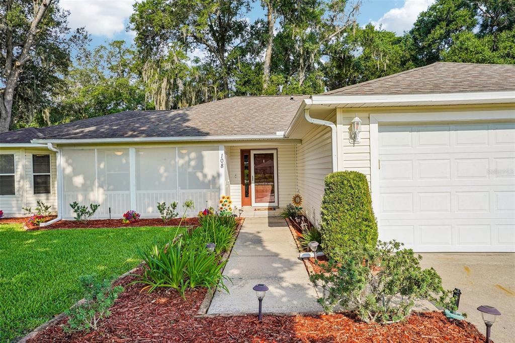 A single-story house features a screened-in porch, a concrete walkway, and a white garage door — 108 CHERRY BLOSSOM LANE, LADY LAKE, FL