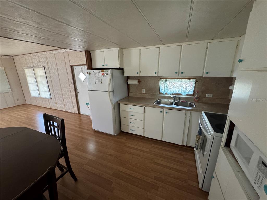A kitchen with white cabinets, laminate countertops, and wood-look flooring opens to a dining area — 1843 SHADY COVE DRIVE, HOLIDAY, FL