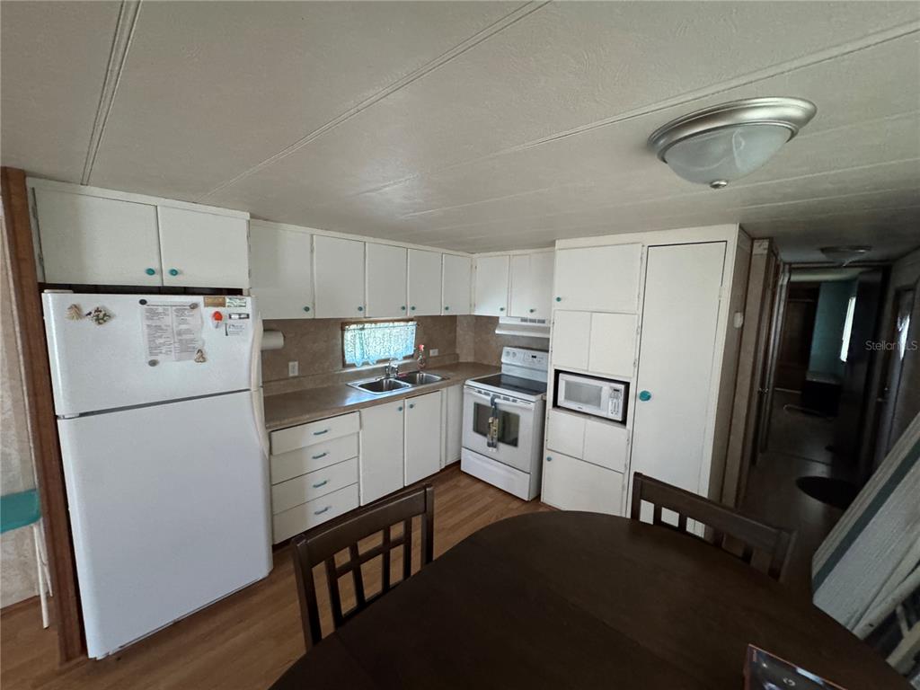 A kitchen with white cabinets, white appliances, and a wooden dining table in the foreground — 1843 SHADY COVE DRIVE, HOLIDAY, FL