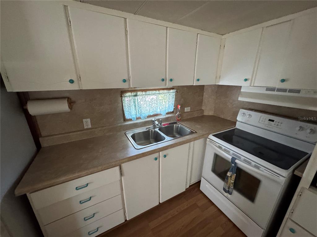 A kitchen features white cabinets, a double sink, laminate countertops, and a white electric stove — 1843 SHADY COVE DRIVE, HOLIDAY, FL