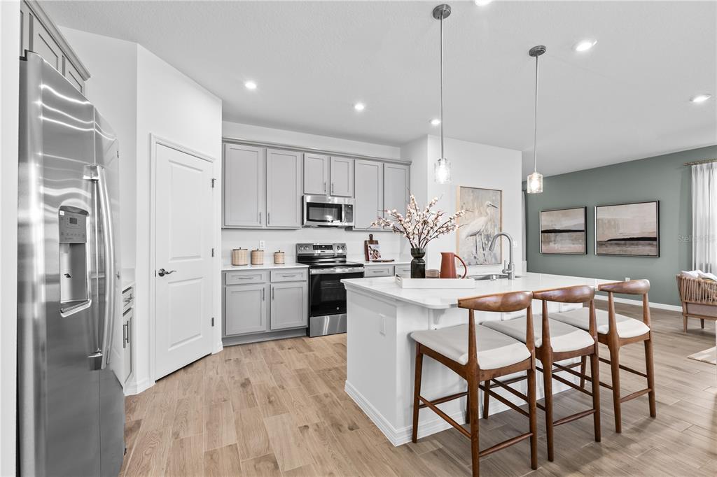 A modern kitchen features gray cabinets, a white island with bar seating, and stainless appliances — 10176 MORNING MEADOWLARK TRAIL, PARRISH, FL