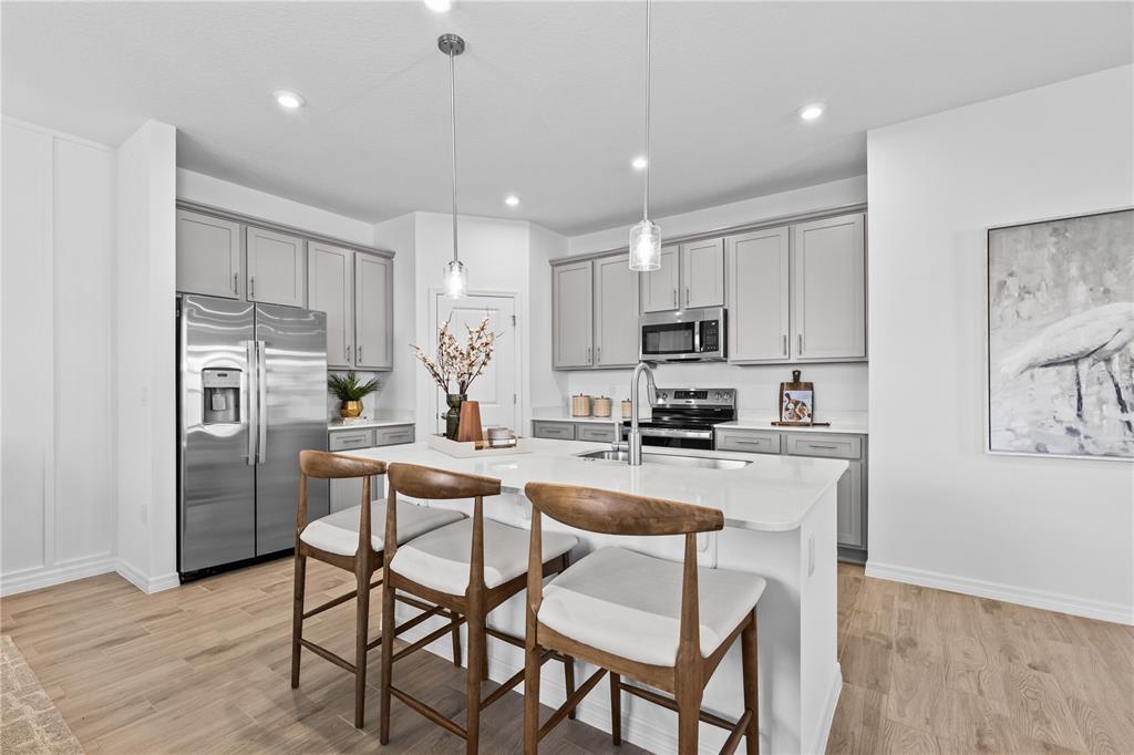 A modern kitchen features light gray cabinets, stainless steel appliances, and a central island — 10176 MORNING MEADOWLARK TRAIL, PARRISH, FL
