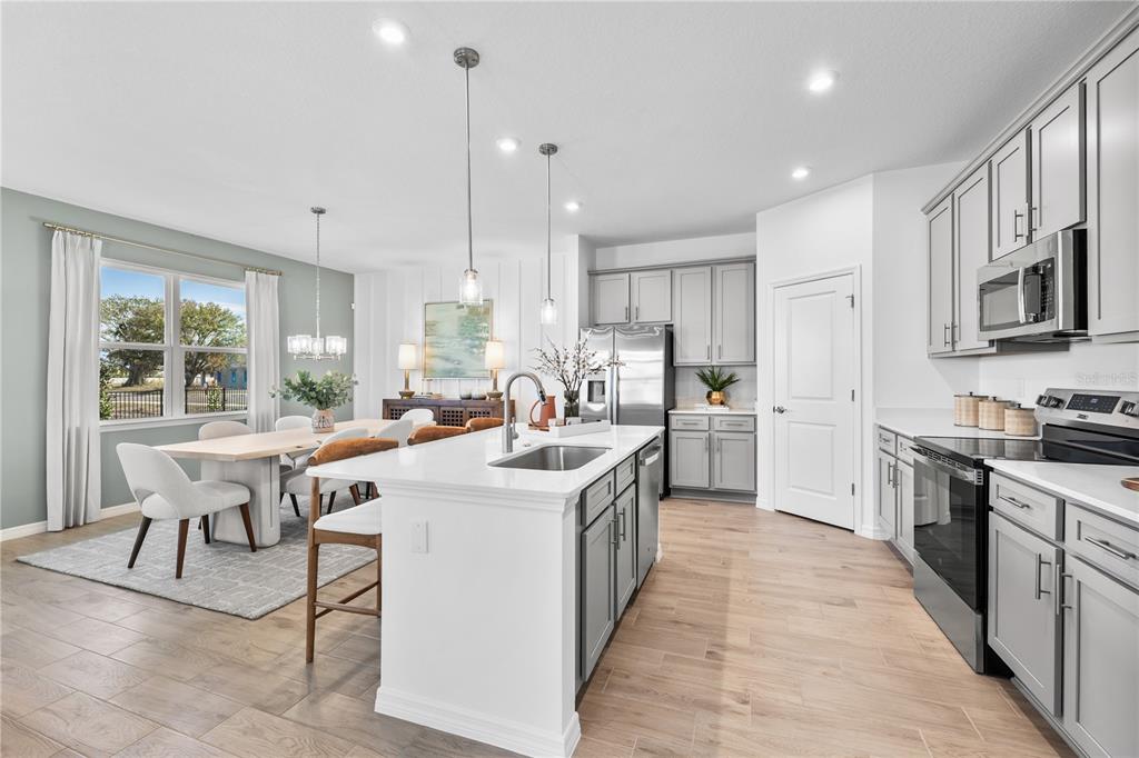 A modern kitchen with gray cabinets, white countertops, and an island opens to a dining area — 10176 MORNING MEADOWLARK TRAIL, PARRISH, FL