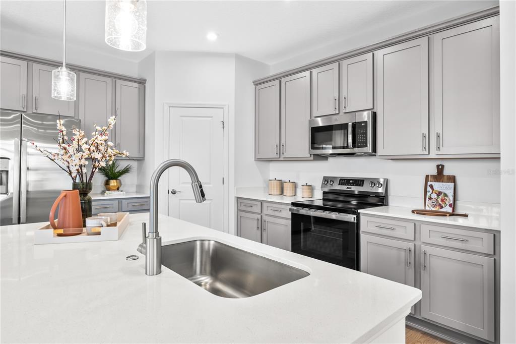 A kitchen features gray cabinets, white countertops, a stainless steel sink, and stainless steel appliances — 10176 MORNING MEADOWLARK TRAIL, PARRISH, FL