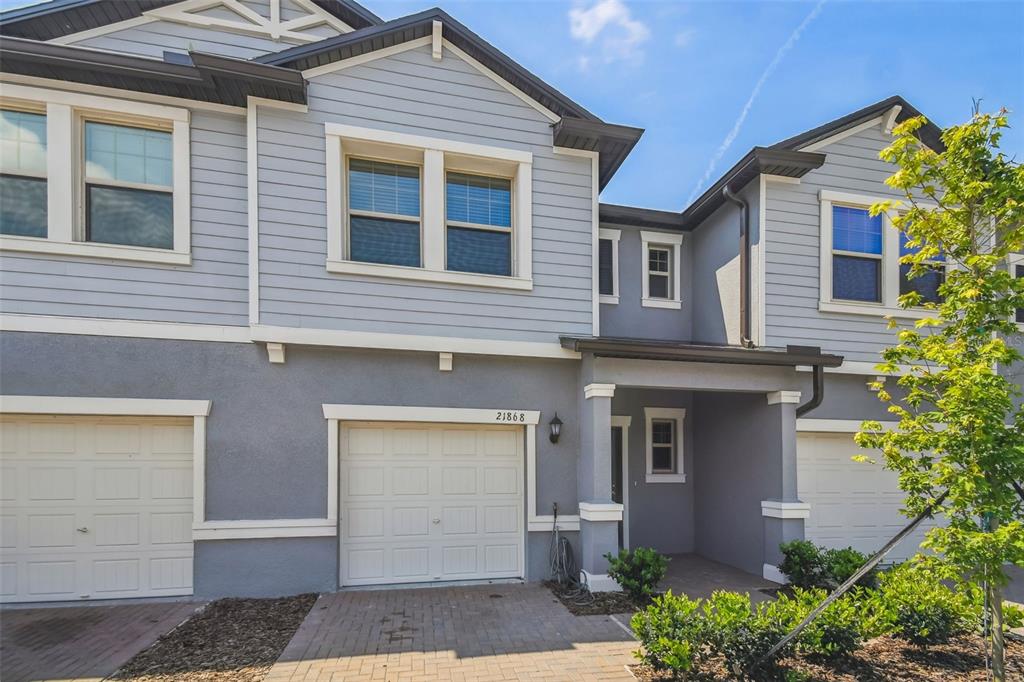 A two-story townhouse exterior features gray siding, a paved driveway, and a single-car garage — 21868 LYONIA LANE, LAND O LAKES, FL