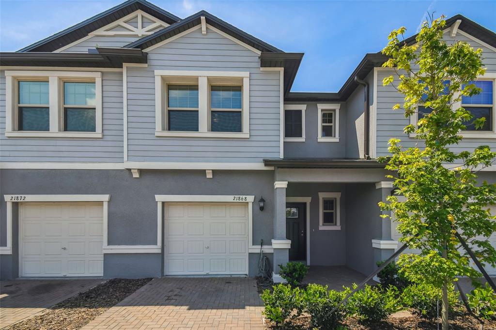 A two-story townhouse exterior features gray siding, a paved driveway, and two garage doors — 21868 LYONIA LANE, LAND O LAKES, FL