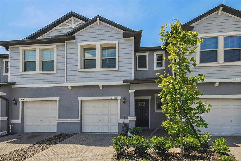 The exterior of a multi-unit townhouse features light blue siding, gray stucco, and white garage doors — 21868 LYONIA LANE, LAND O LAKES, FL