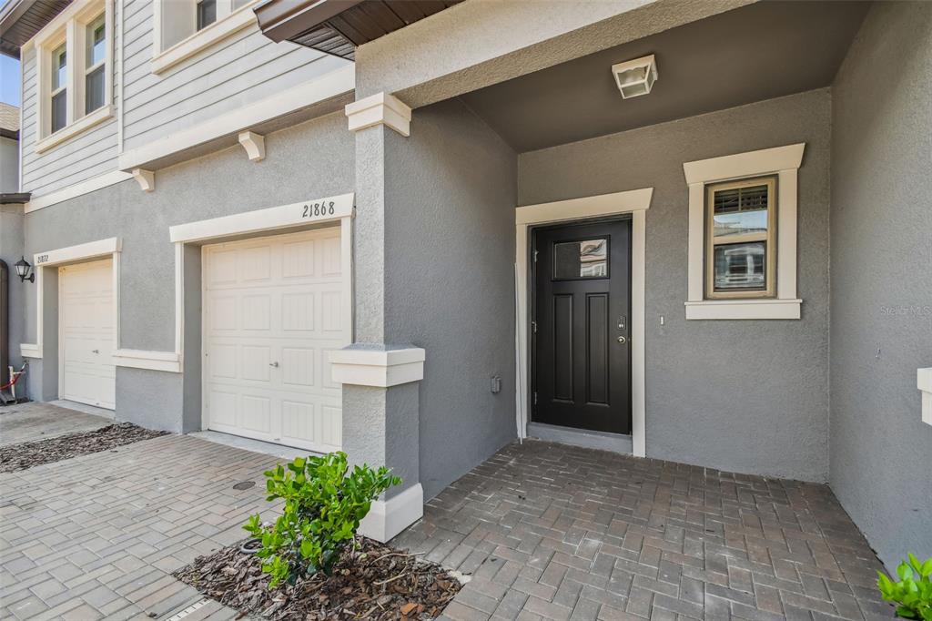 The exterior of a gray townhouse features a black front door and a white garage — 21868 LYONIA LANE, LAND O LAKES, FL
